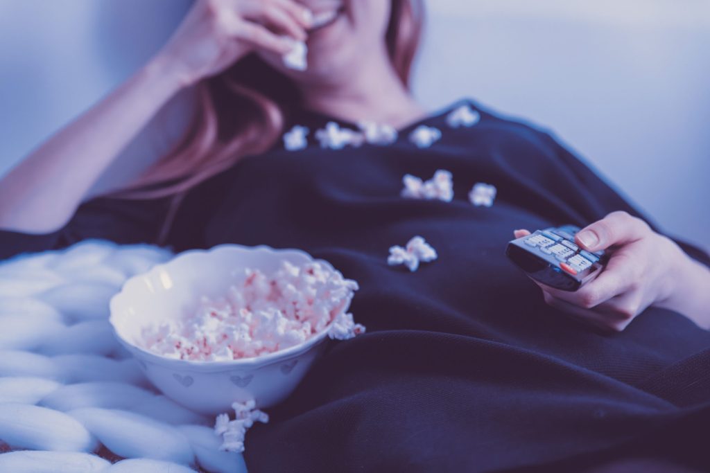 Vrouw kijkt tv en eet popcorn. 