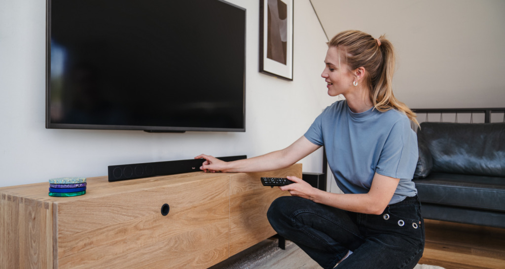 Vrouw zit voor de tv met daaronder de CINEBAR 11 en stelt deze in.