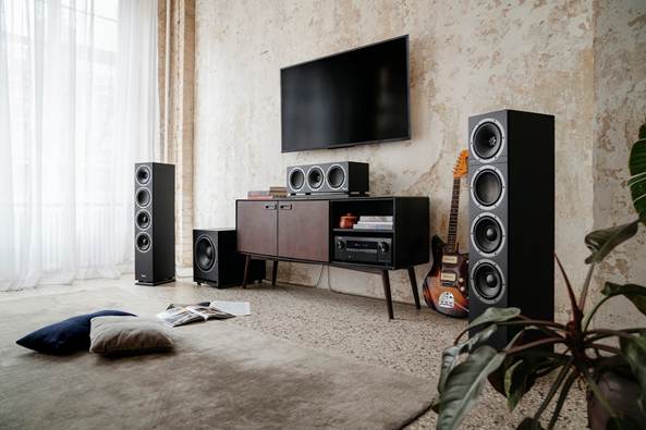 Afbeelding van twee THEATER 500-speakers, THEATER-centerspeaker en een S 6000-subwoofer in een woonkamer achtergrond met een TV en gitaar.
