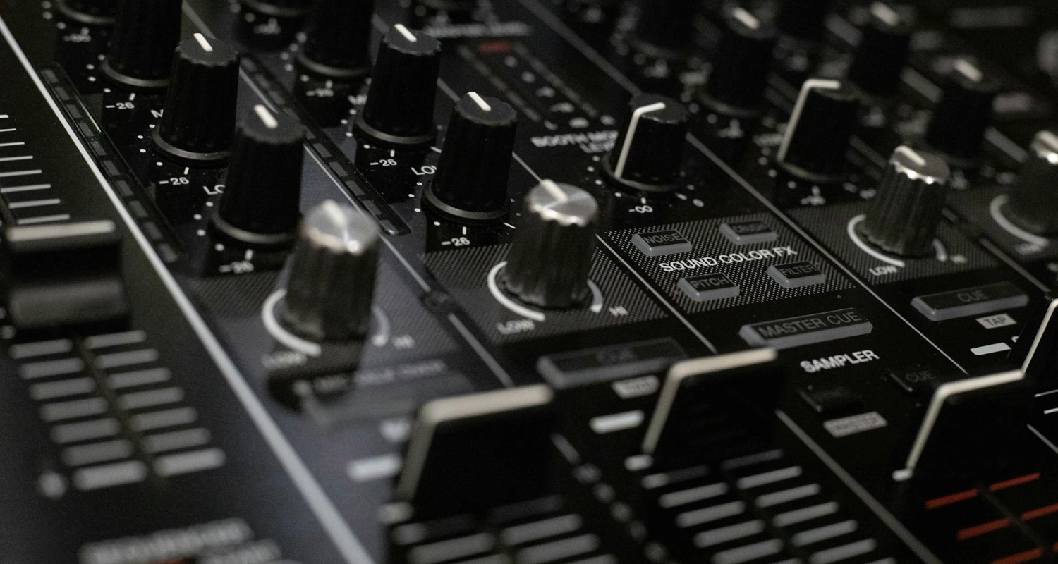Nahaufnahme eines DJ-Mixers mit Reglern, Knöpfen und Fadern, die für Klangmischung und Soundeffekte genutzt werden.